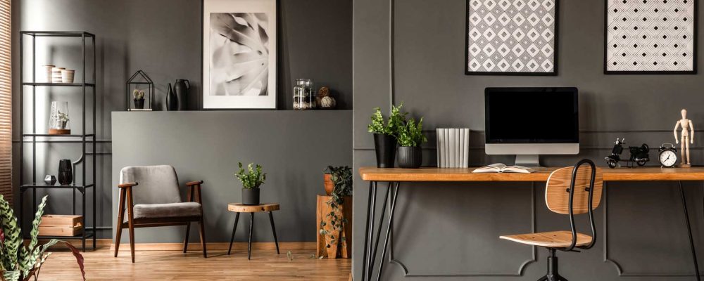 Patterned posters above desk with computer monitor in grey home office interior with plants